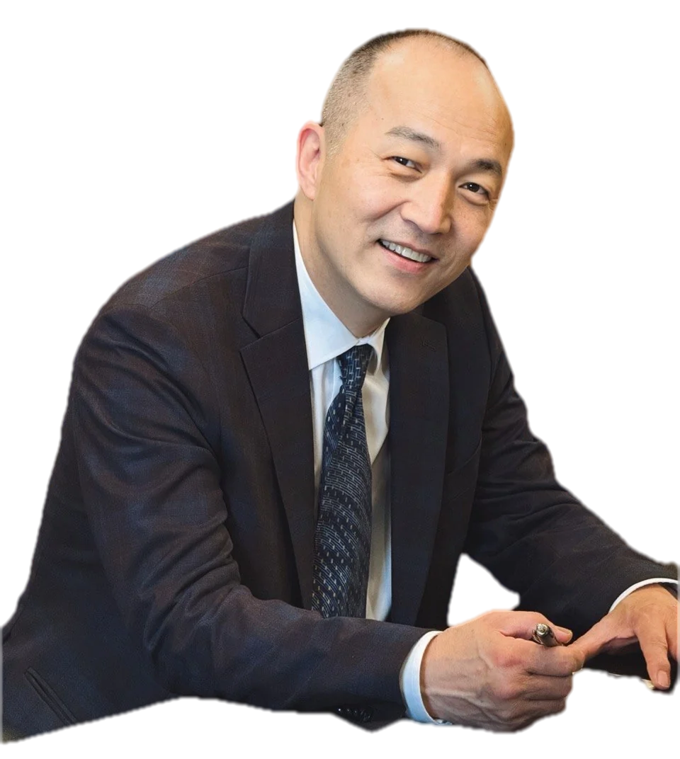 Grand Master Won Kuk Kim, smiling, seated at a desk with a pen in his hand