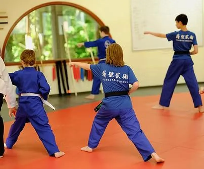 Young students in blue uniforms practising a stance together at the academy