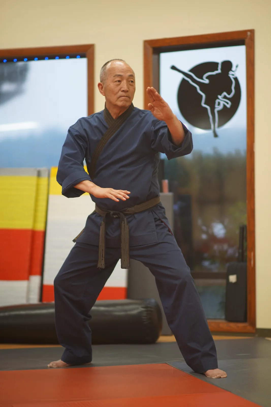 Grand Master Won Kuk Kim holding an open-hand guard stance on the red mats at the academy