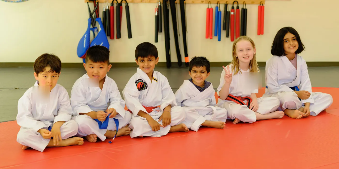 Six young students in white uniforms sitting on the red mat, smiling