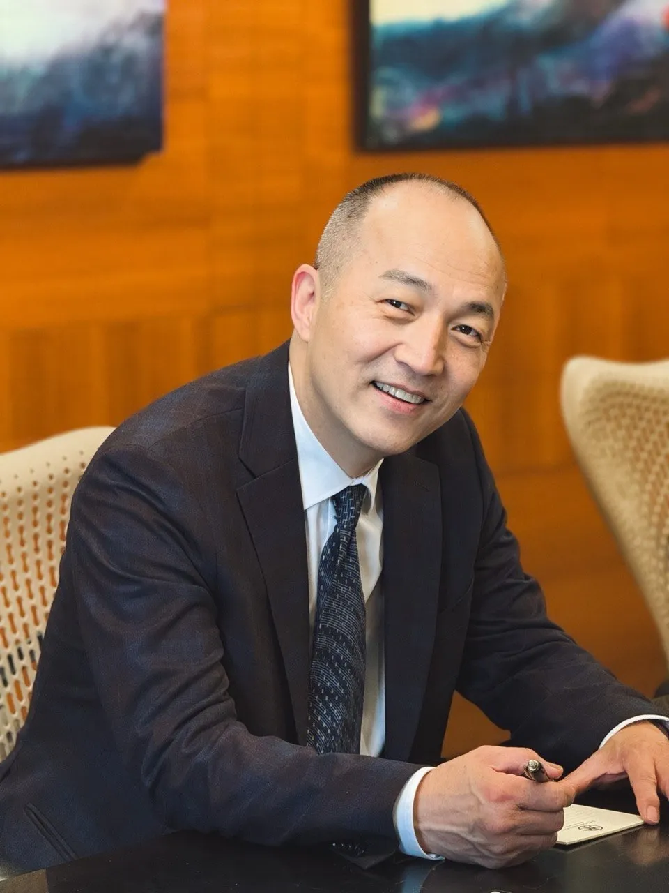Grand Master Won Kuk Kim in a suit, smiling, seated at a desk with a pen in hand