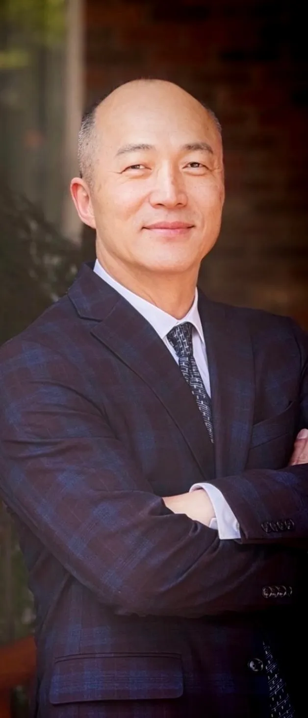 Grand Master Won Kuk Kim in a navy suit and tie, arms crossed, smiling