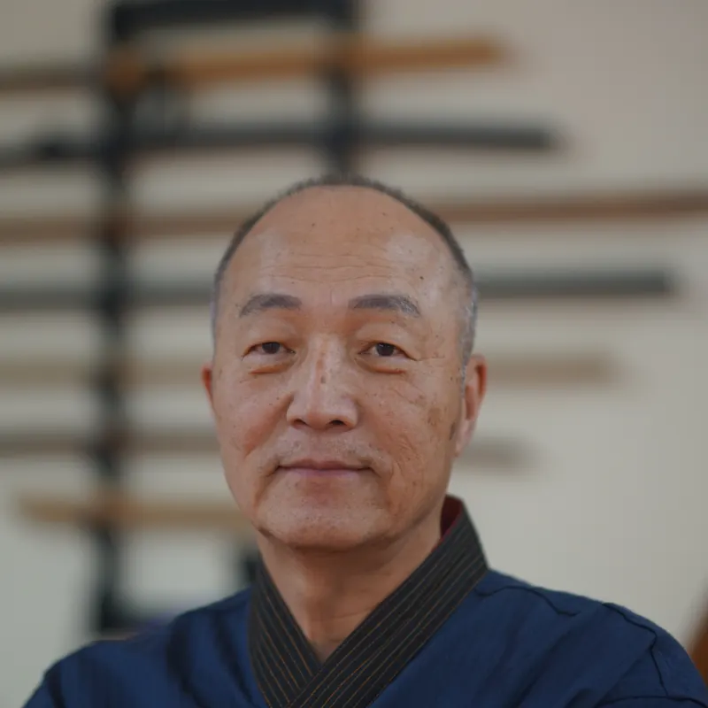 Front portrait of Grand Master Won Kuk Kim, the weapon rack softly blurred behind him