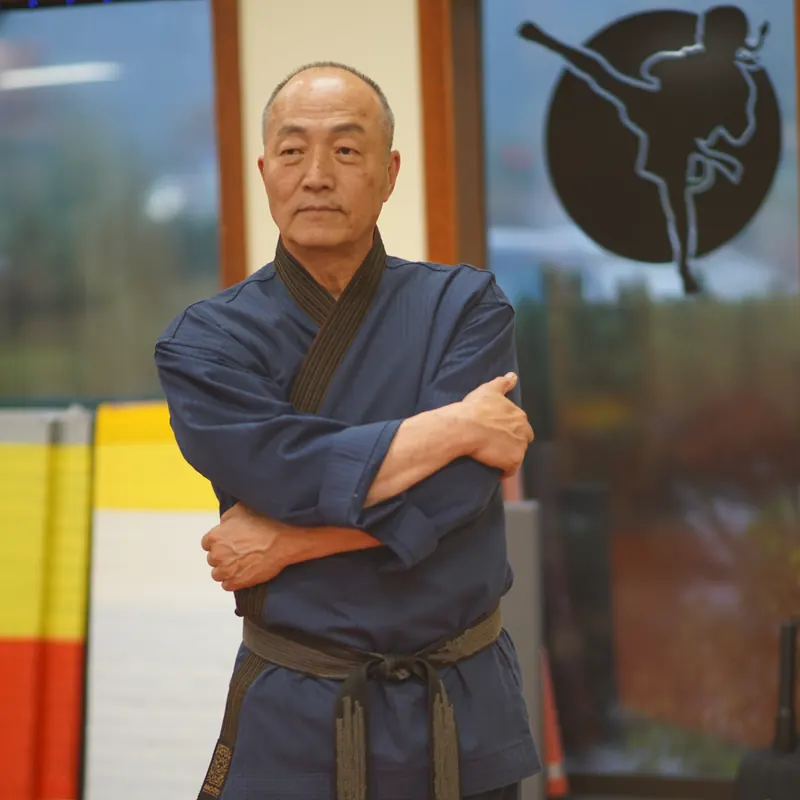 Grand Master Won Kuk Kim standing with arms crossed in the academy