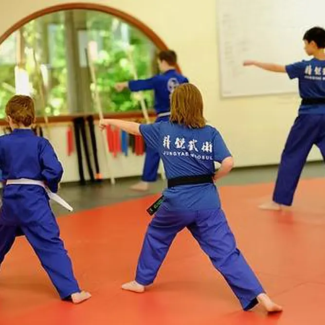 Young students in blue uniforms practicing a stance in the academy