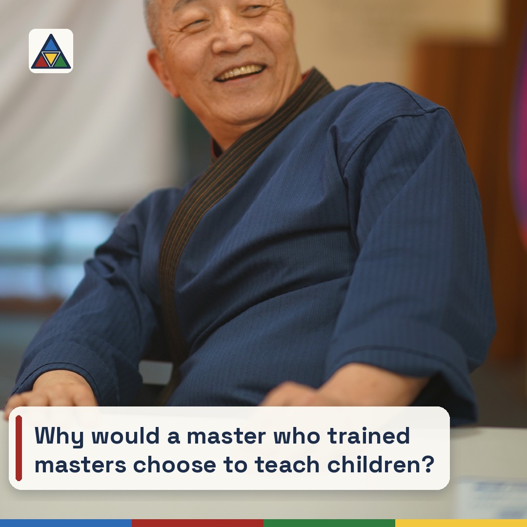 Grand Master Won Kuk Kim laughing, seated at a table in the academy, in a navy dobok