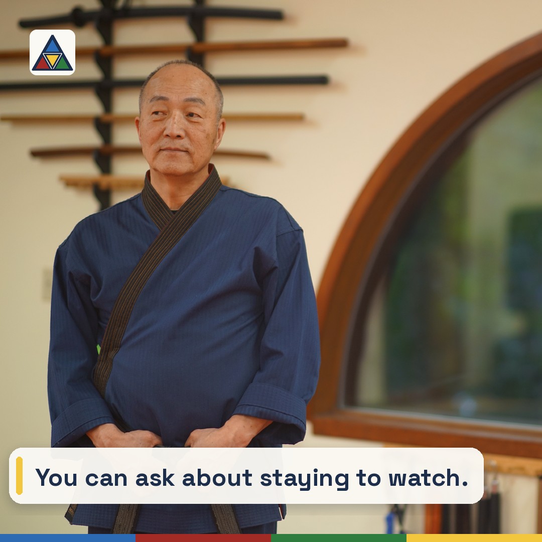 Grand Master Won Kuk Kim with hands clasped beside an arched window and the weapon rack